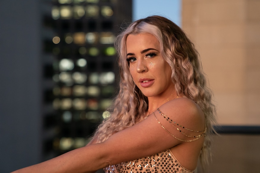 Woman wearing sequin dress, on balcony at dusk.