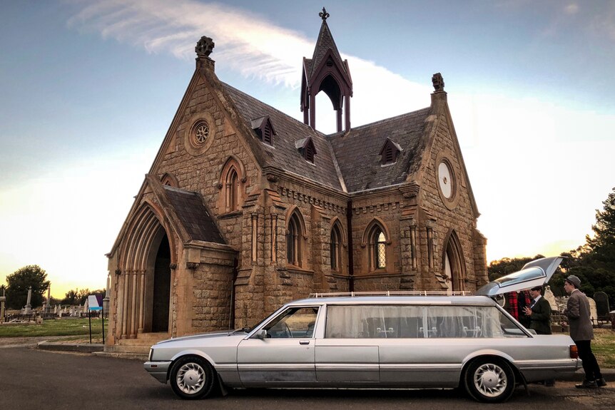 A funeral hearse at the Bendigo cemetery parked in front of a church.