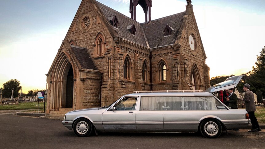 A funeral hearse at the Bendigo cemetery parked in front of a church.