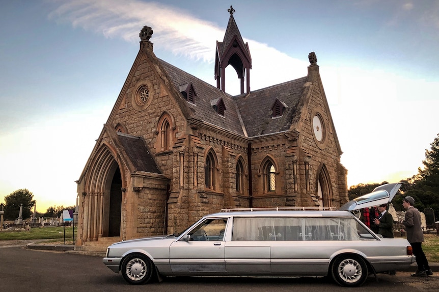 A funeral hearse at the Bendigo cemetery parked in front of a church.