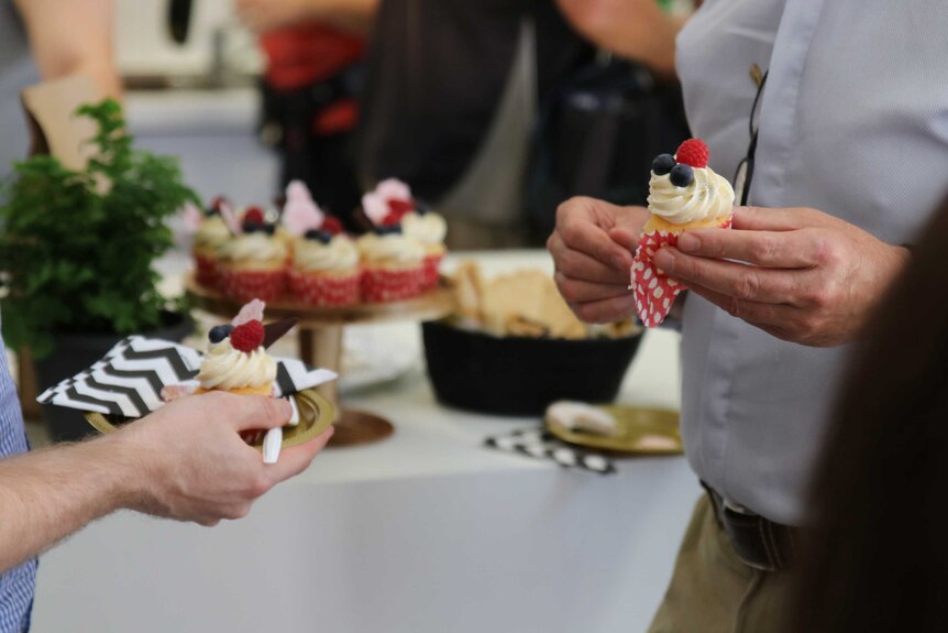 People holding fruit-topped Banksia Beans Cafe cupcakes which have been baked by detainees.