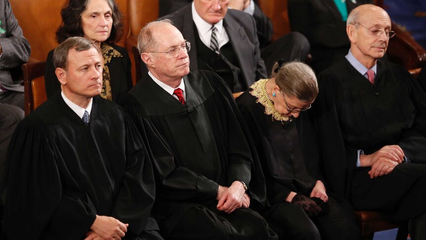 Ruth Bader Ginsburg with her head bowed down while sitting next to other Supreme Court Justices.