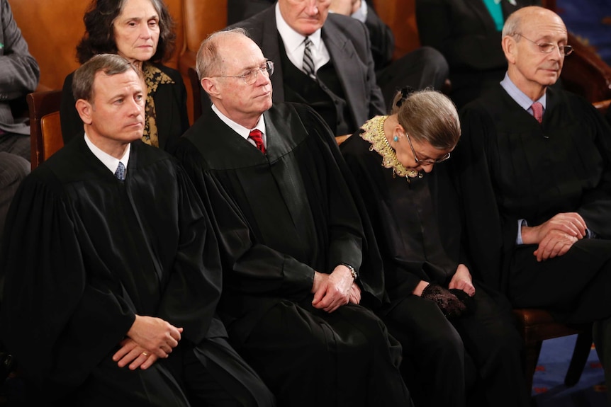 Ruth Bader Ginsburg with her head bowed down while sitting next to other Supreme Court Justices.