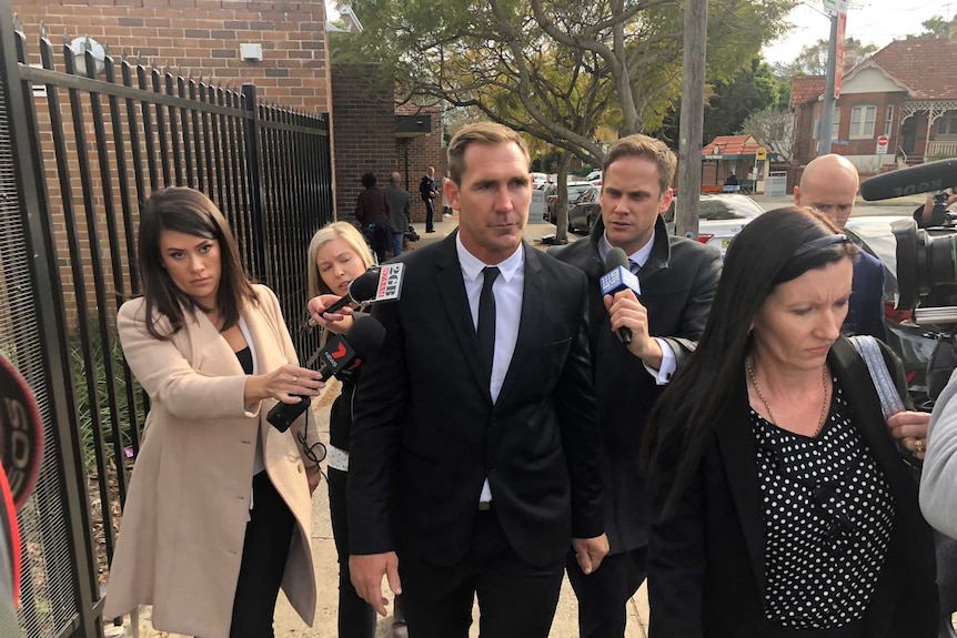 man in suit surrounded by media on street