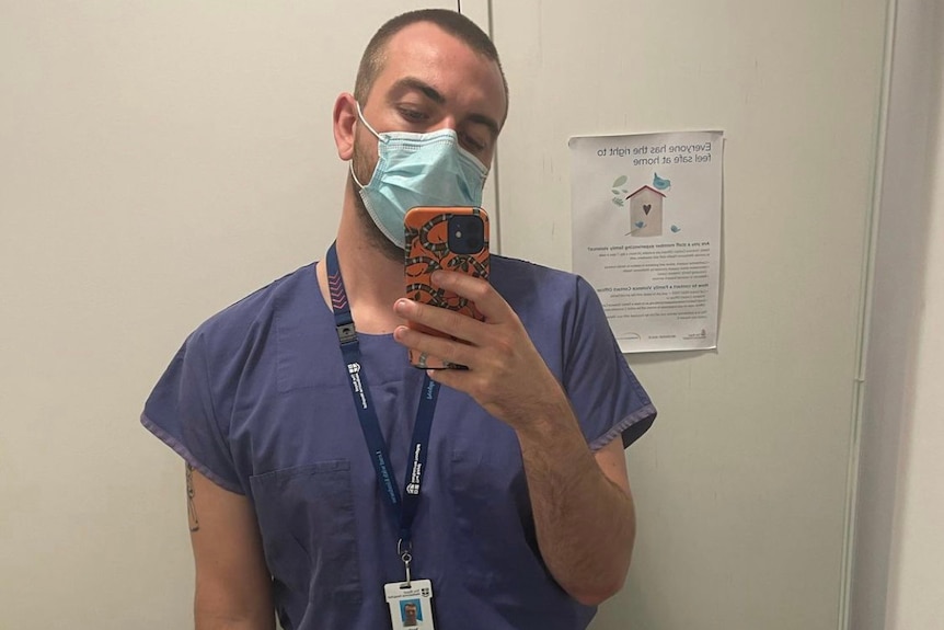 A man in blue medical scrubs taking a selfie on his phone