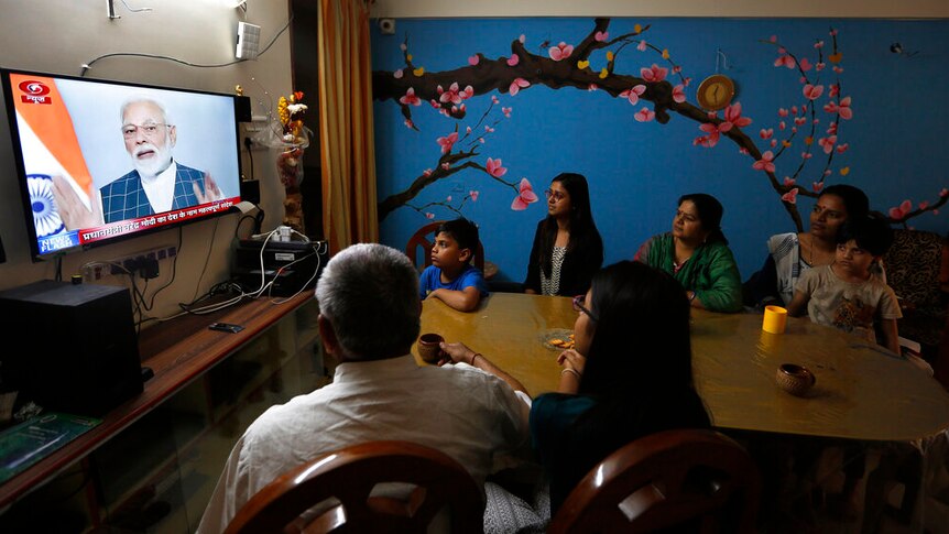A family sitting around a television with featuring the face of Narendra Modi.