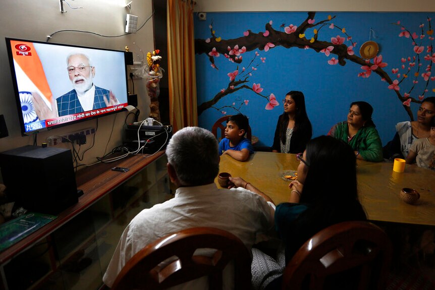 A family sitting around a television with featuring the face of Narendra Modi.