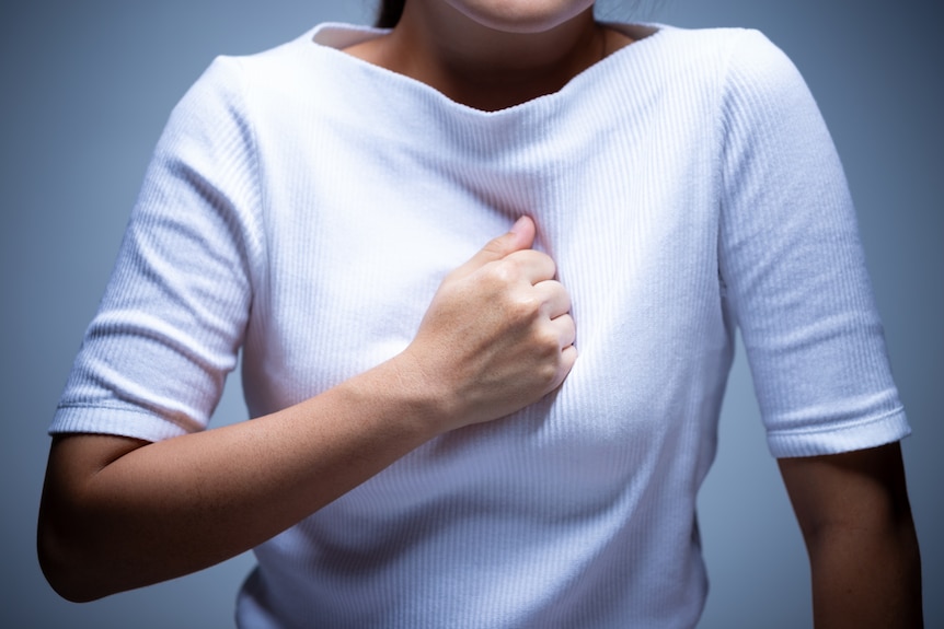 Closeup of the torso of a woman who is pressing her fist into her breastbone.