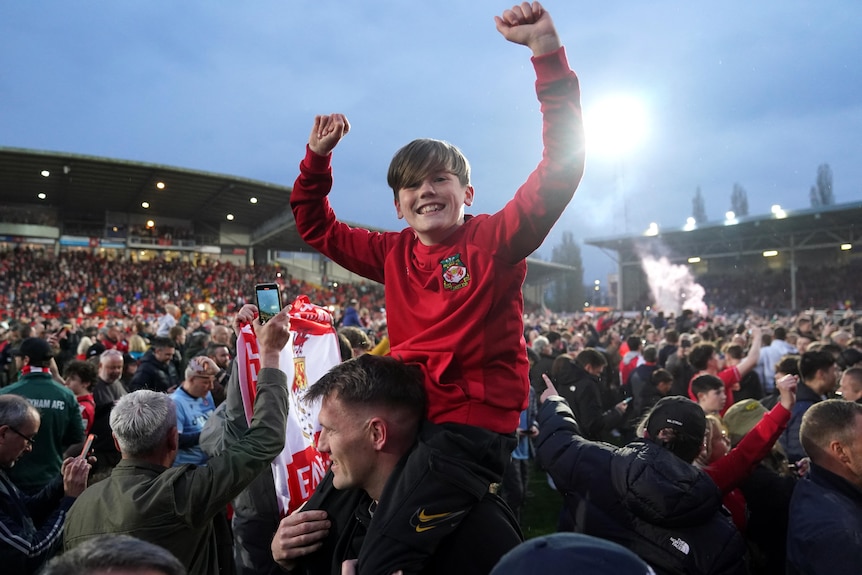 A young boy on an adult's shoulders puts his hands in the air to celebrate Wrexham winning the National League.