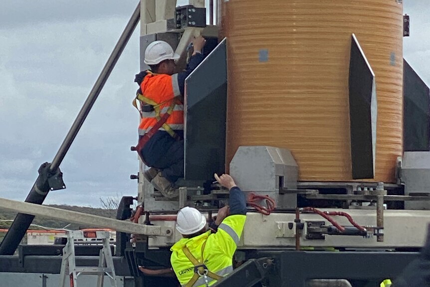 Two technicians working on a round tank-like structure, the bottom of the rocket