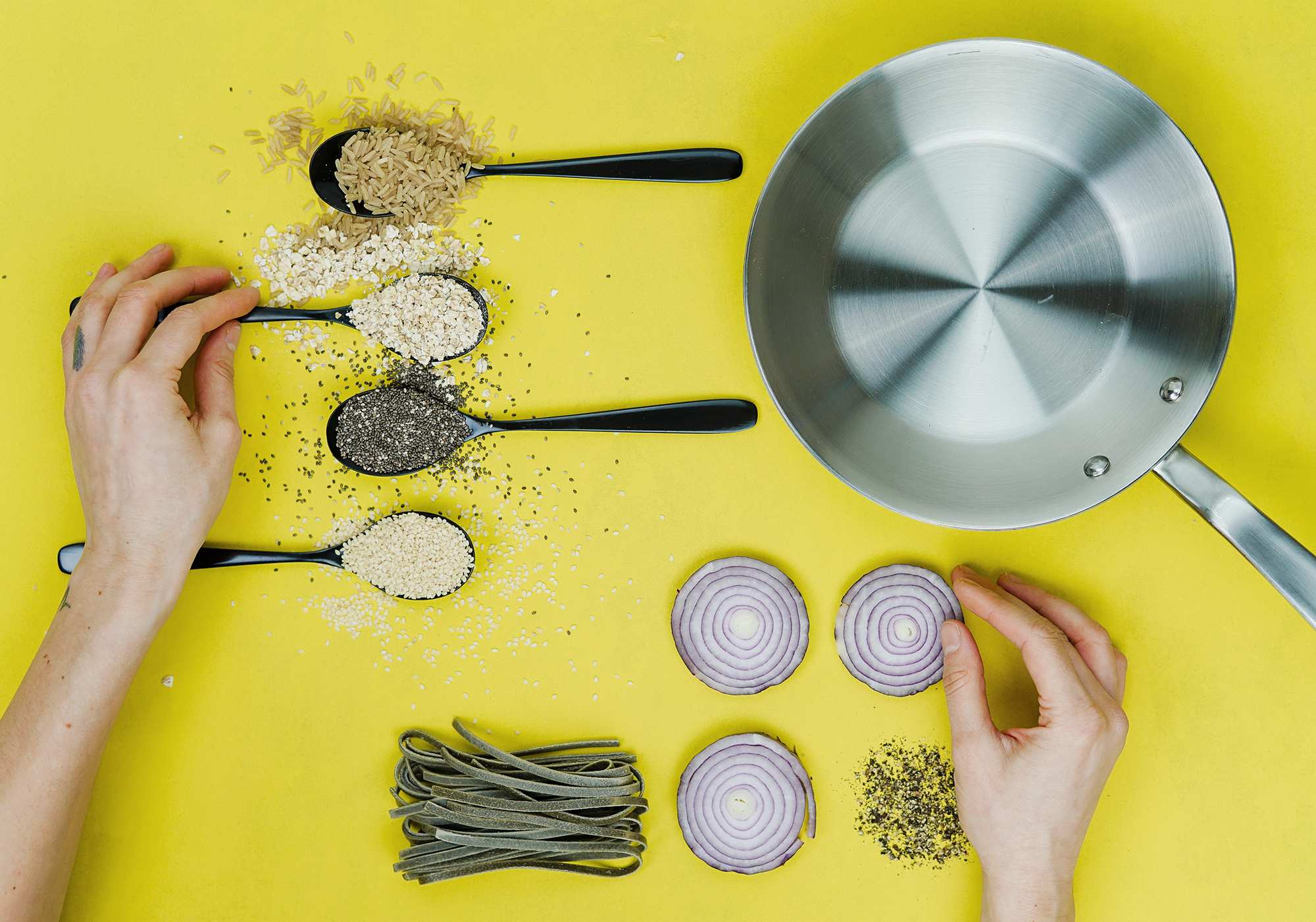 Flatlay with hands, onion slices, pasta, pepper and grains lined up to depict the organisation the meal planning requires.