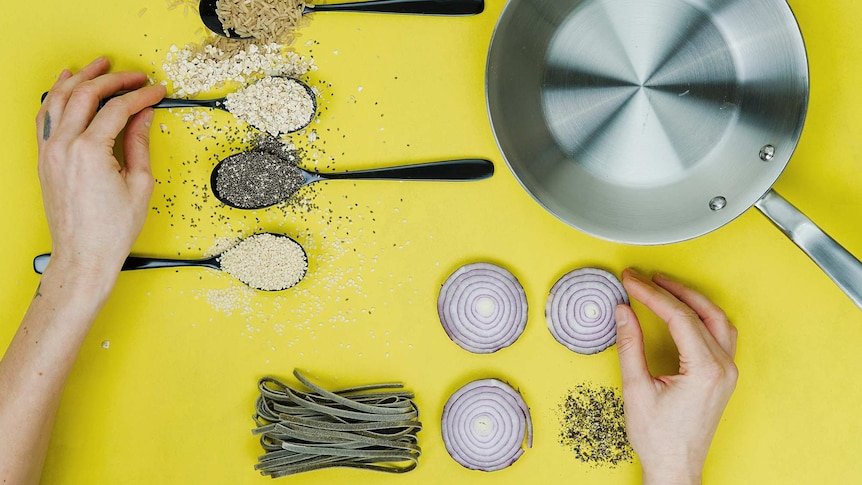 Flatlay with hands, onion slices, pasta, pepper and grains lined up to depict the organisation the meal planning requires.