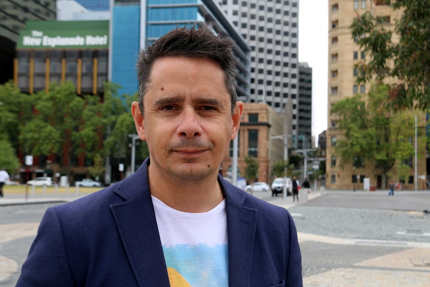 Headshot of ben Wyatt looking dapper with a city background.