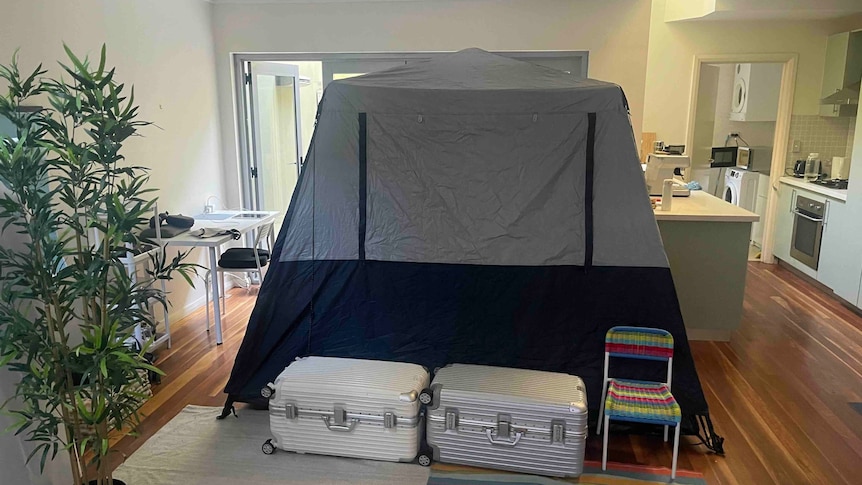 Grey and black tent in living room, surrounded by two suitcases and a plastic chair.