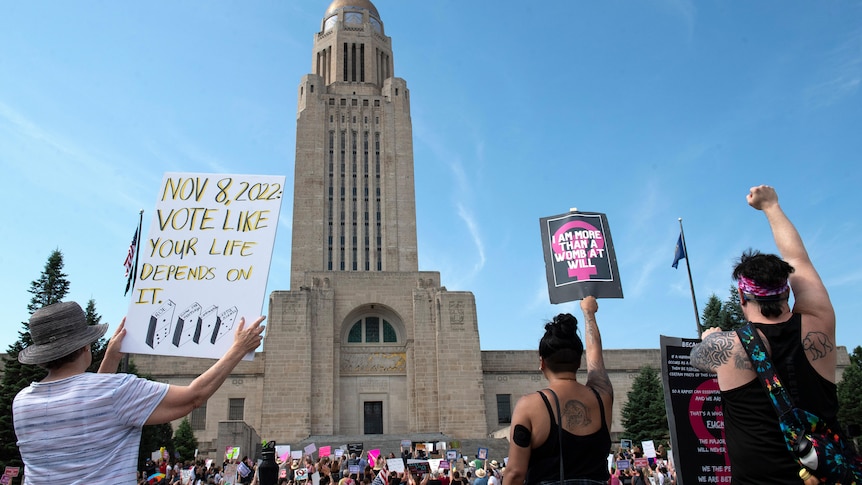 A large tower is pictured with protesters in front of it, fists in the sky, holding signs during an Abortion Rights Rally