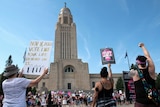 A large tower is pictured with protesters in front of it, fists in the sky, holding signs during an Abortion Rights Rally