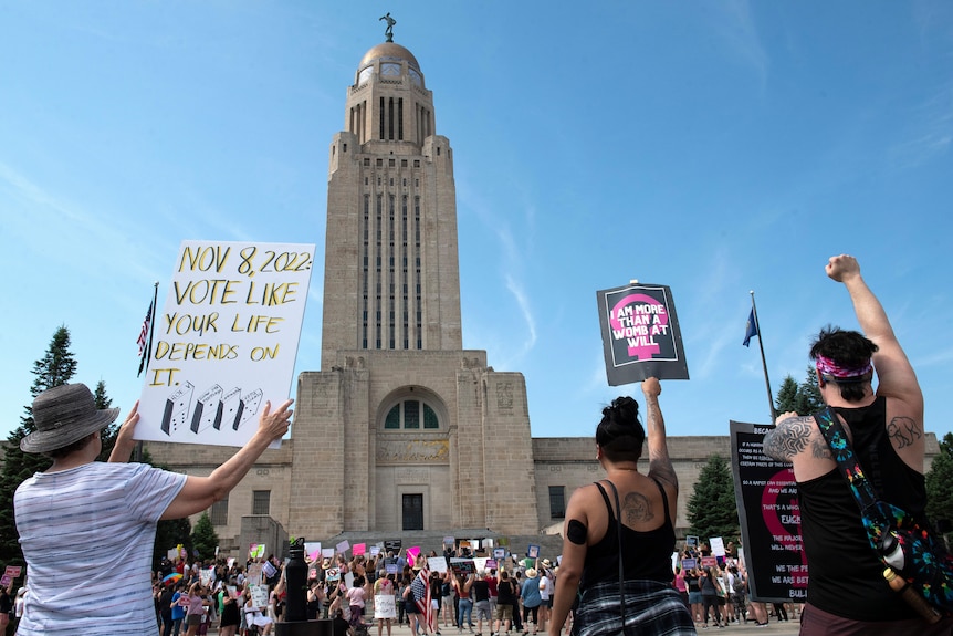 Une grande tour est photographiée avec des manifestants devant elle, les poings dans le ciel, tenant des pancartes lors d'un rassemblement pour le droit à l'avortement