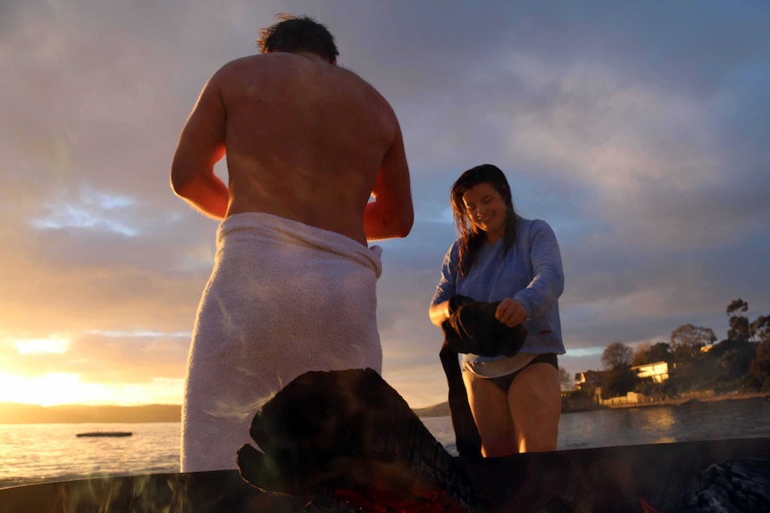 Two winter solstice swimmers warm by a fire.