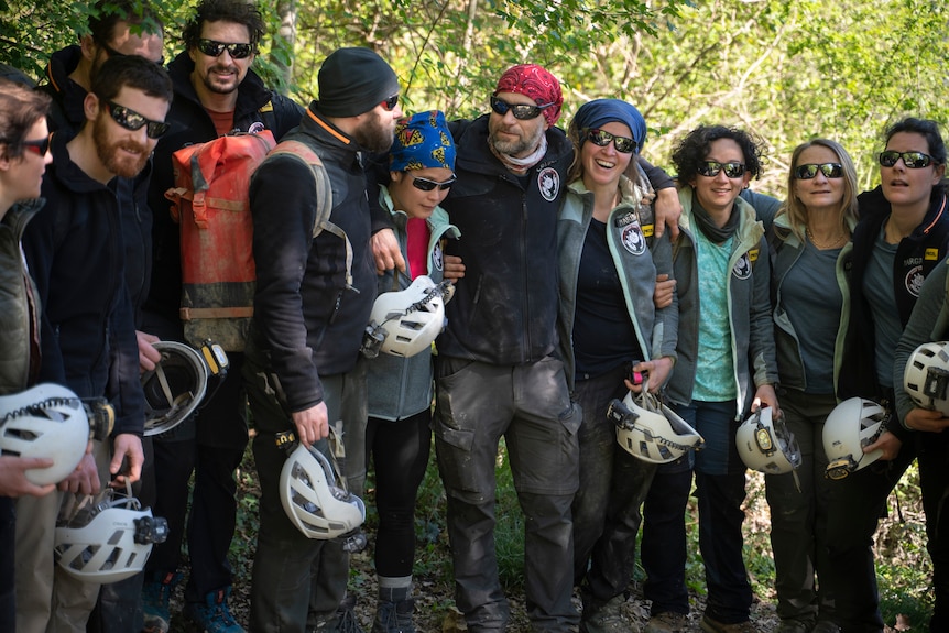 A group in hiking gear hold helmets while posing for a photo