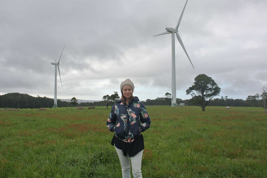 Taryn Lane from Hepburn Wind stands by two of the community-owned turbines at Daylesford, Victoria.