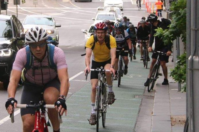 Cyclists riding uphill with morning peak hour traffic driving past them.