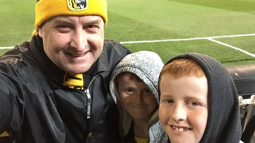 Matt Brown in a tigers beanie with his sons with the MCG in the background.