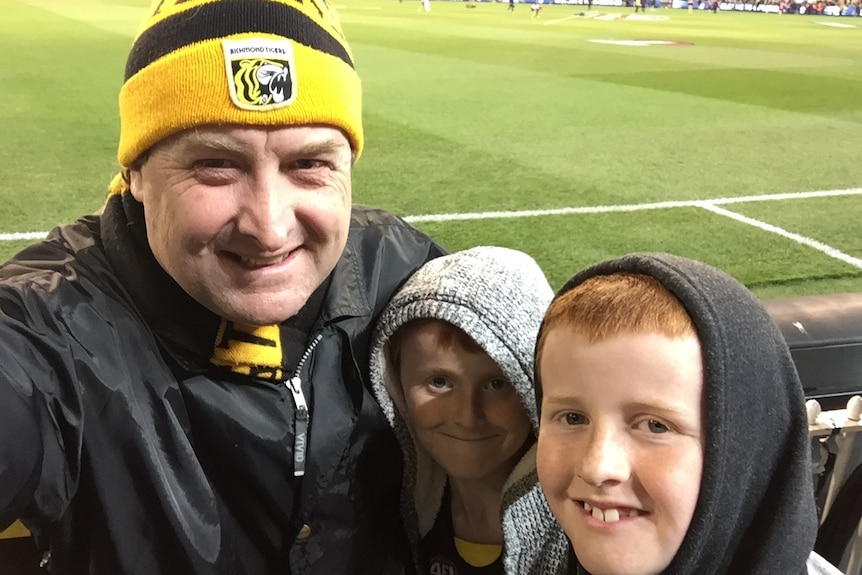 Matt Brown in a tigers beanie with his sons with the MCG in the background.