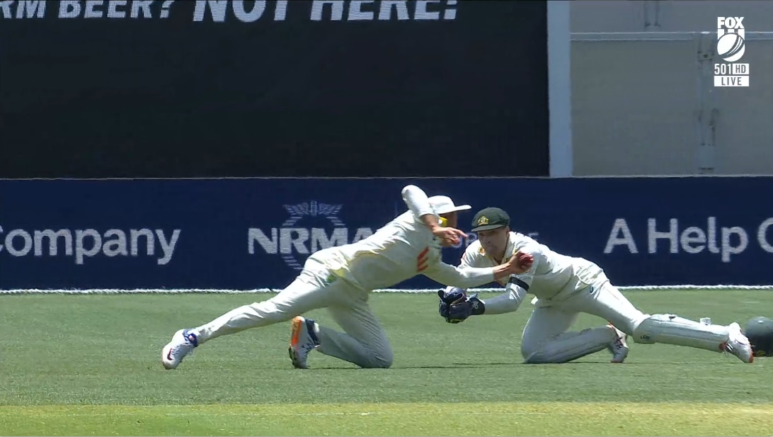 Un jugador de críquet vestido de blanco realiza una atrapada volando bajo con su mano izquierda.