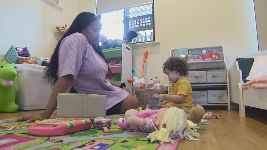 Ms McIntosh and her daughter playing on the floor of her room, surrounded by toys
