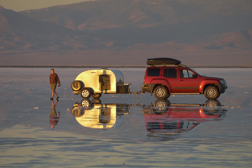 Une personne et une voiture transportant une petite caravane sur un lac