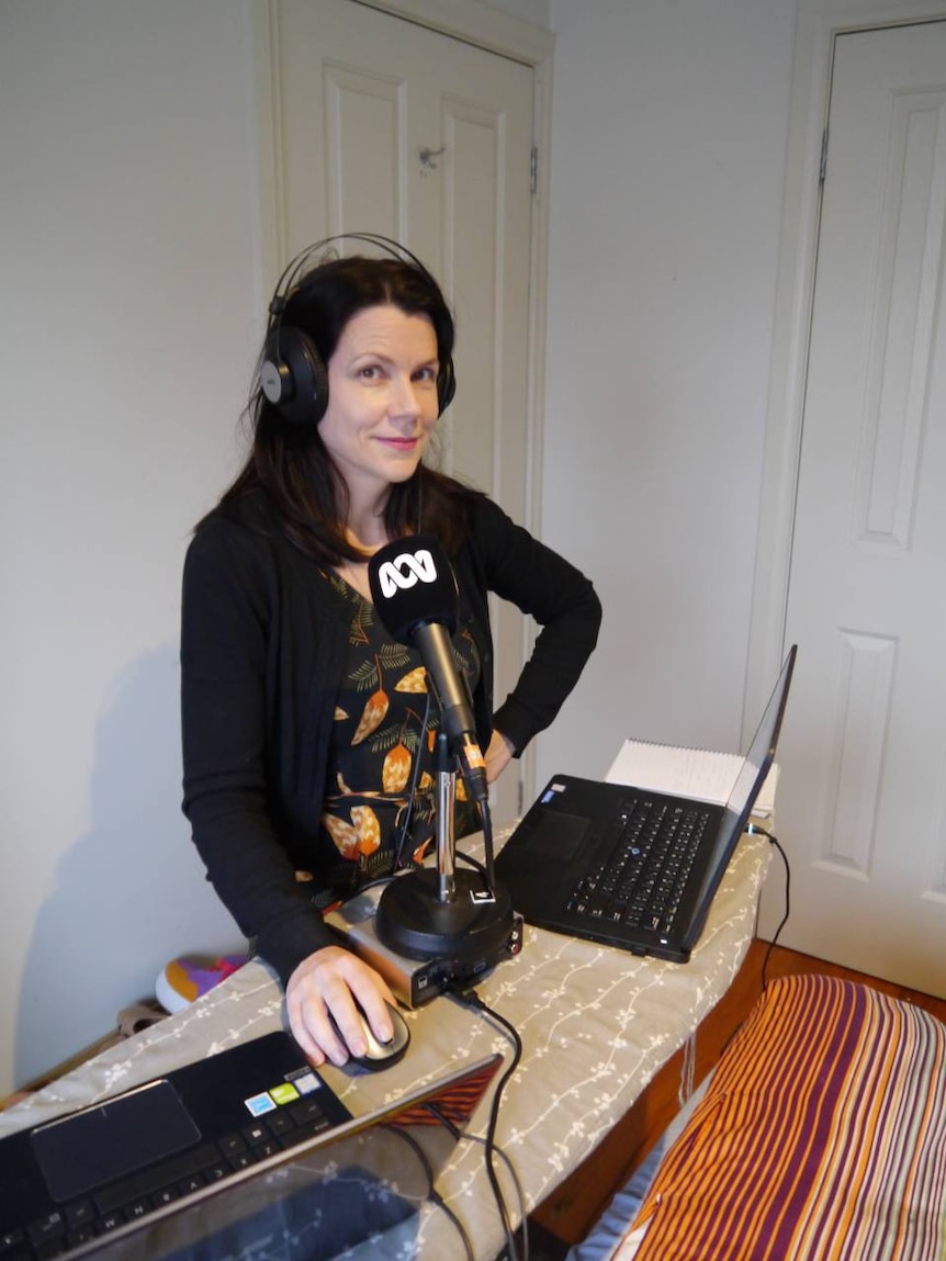 Erica Vowles wears headphones and stands in front of a mic in her makeshift studio from home.
