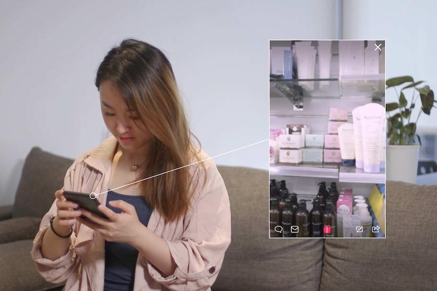 Daigou Yaqiong Hu is texting on her phone with a video featuring various products playing next to her.