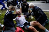 A cyclist with blood on his shirt and his head bandaged is looked after by medical staff on a roadside at the Tour de France.