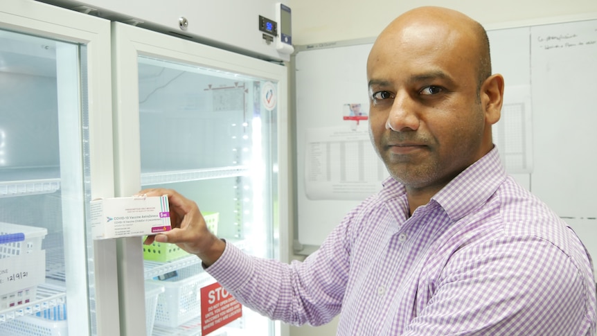 A doctor with a checked shirt holds a box of the Astrazeneca vaccine.