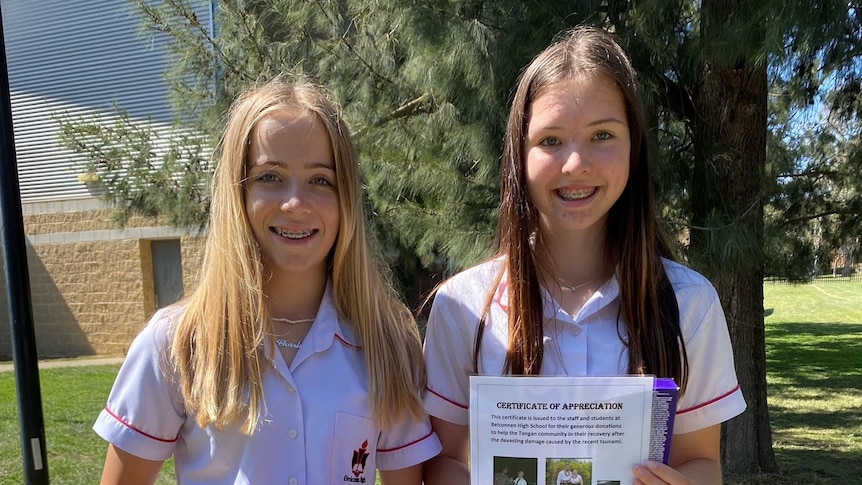 Two girls wearing school uniform hold up donated goods and smile in a parkland