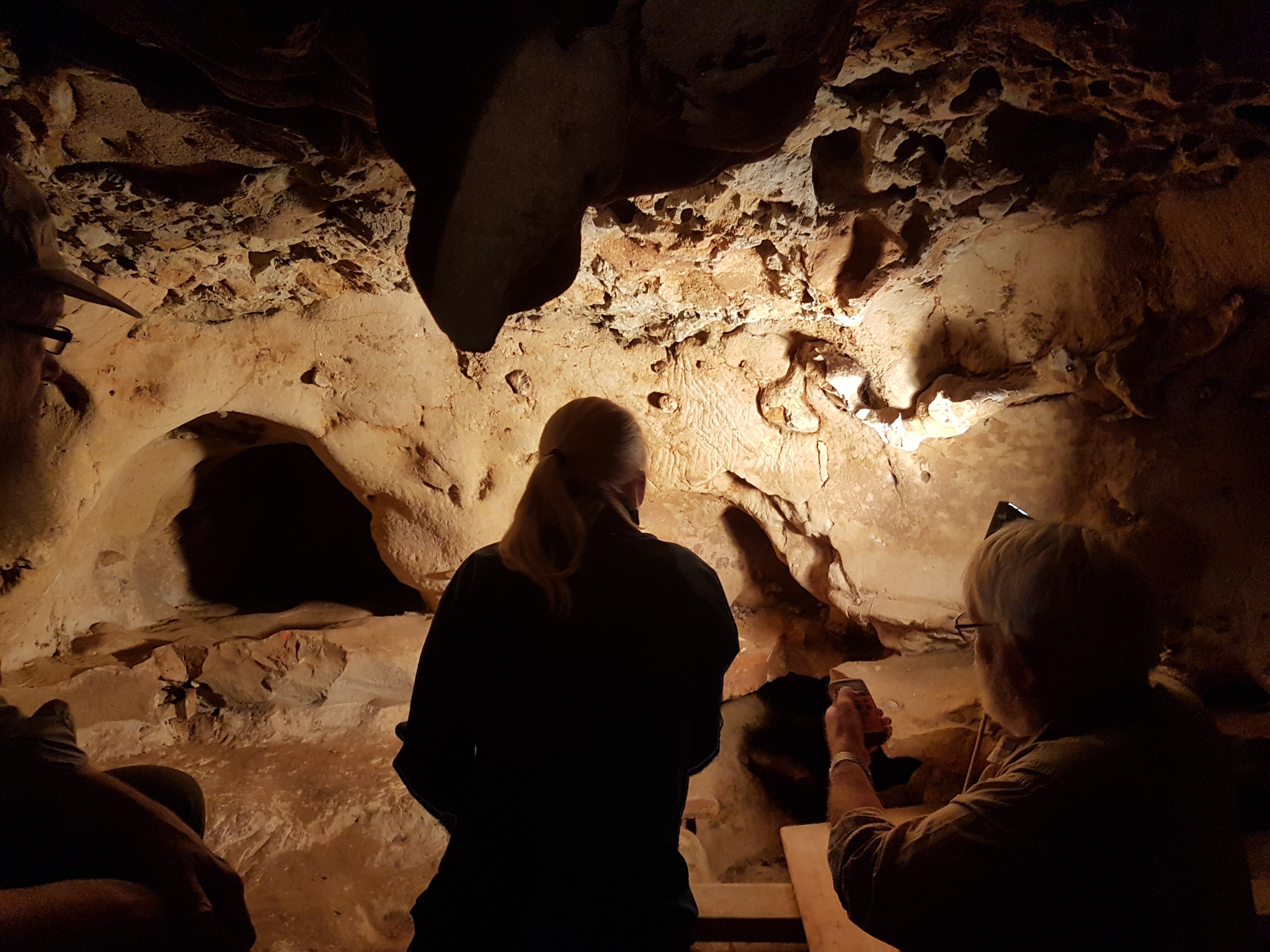 Two people stand in a cave shining a light on etched marks in the rock wall