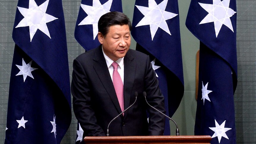 Chinese president speaking in front of four Australian flags
