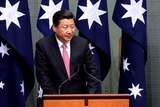 Chinese president speaking in front of four Australian flags