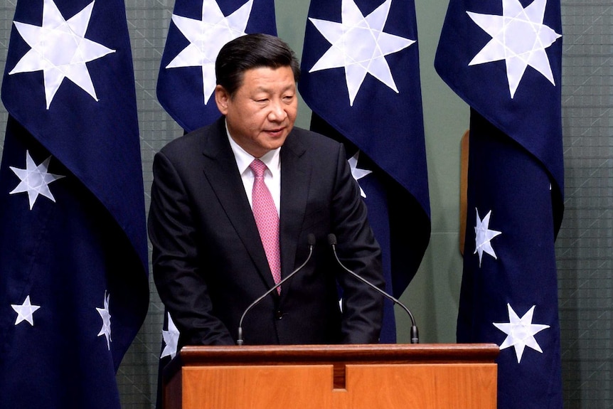 Chinese president speaking in front of four Australian flags