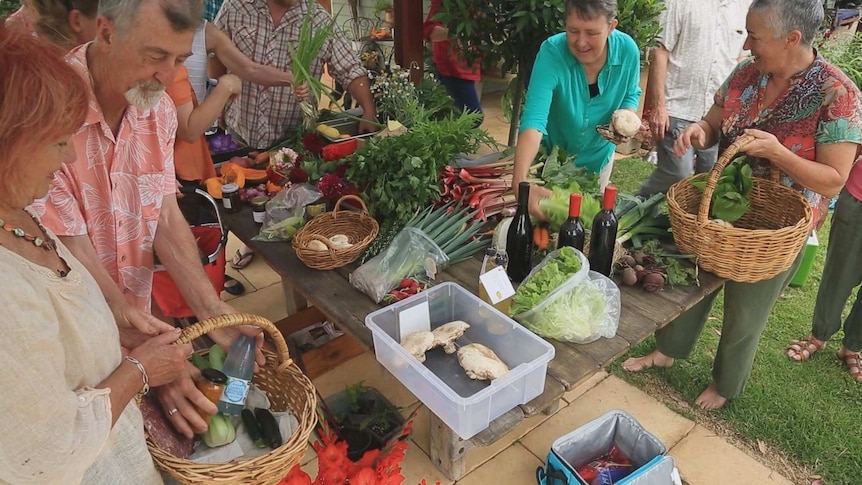 A group of people are busing selecting fresh produce from a table laden with fruit, vegetables and other goodies.