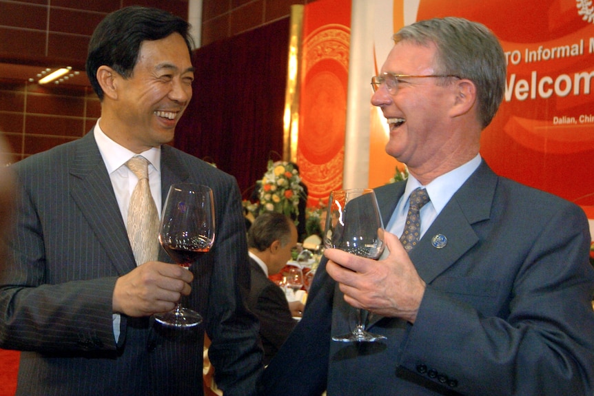 Bo Xilai grips a glass of wine and laughs with a man in a suit 