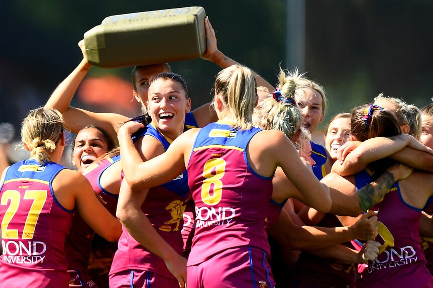 A group of Brisbane Lions AFLW players cheer and embrace after winning a grand final.