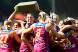 A group of Brisbane Lions AFLW players cheer and embrace after winning a grand final.