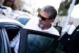 A close-up shot of Daniel Martin Torrijos getting into a car, wearing sunglasses and a white shirt.