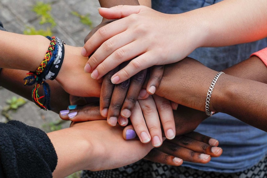 Teenagers of diverse backgrounds have the hands piled one on top of another.