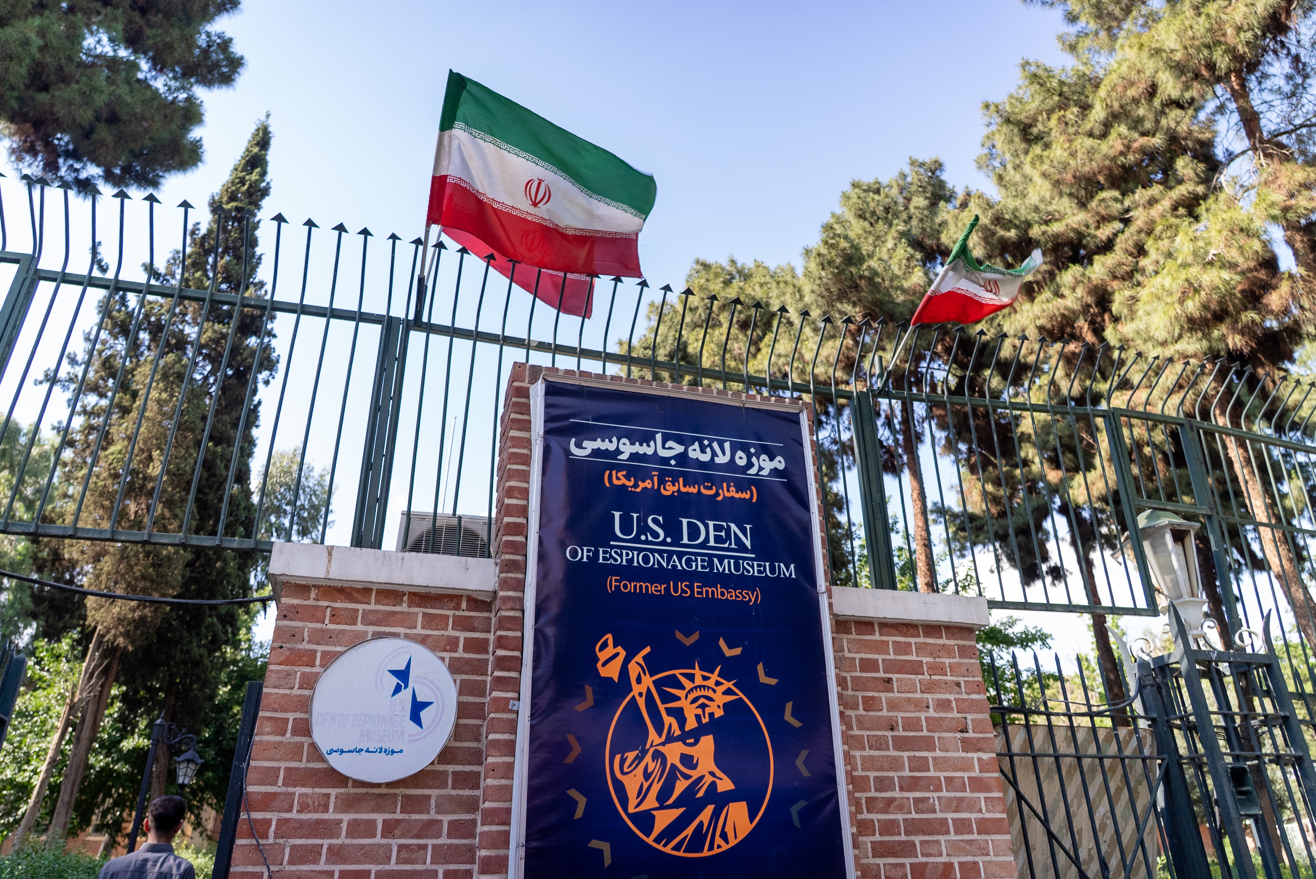 A blue sign in front of a securely fenced wall depicts a shattered Statue of Liberty.