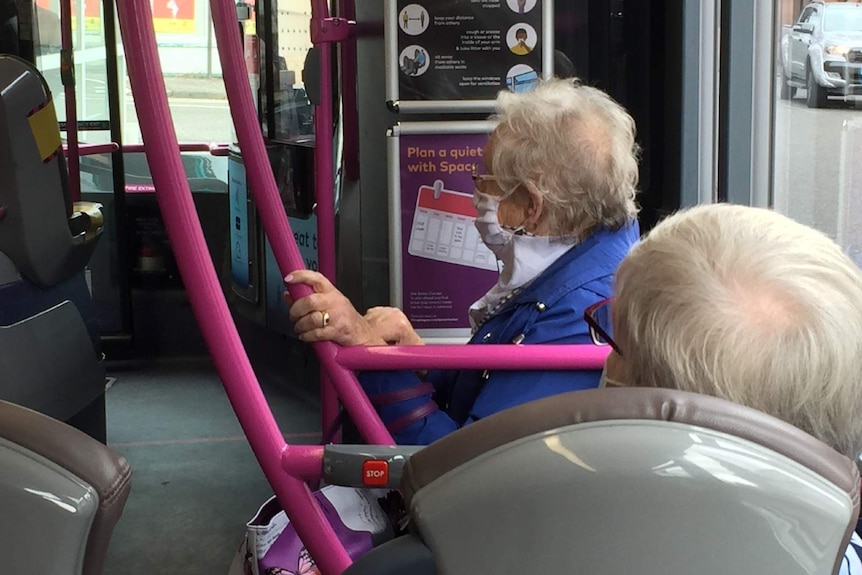 An older woman sits on a bus with a facemask on