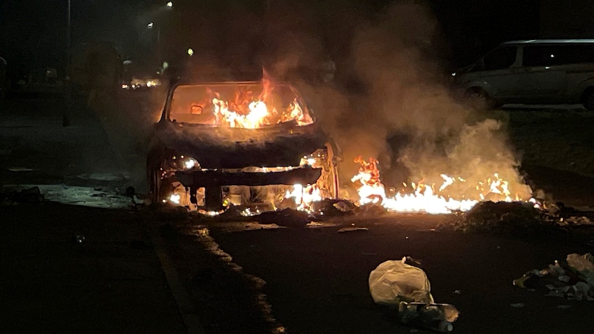 A car is ablaze in the middle of a road at night. 