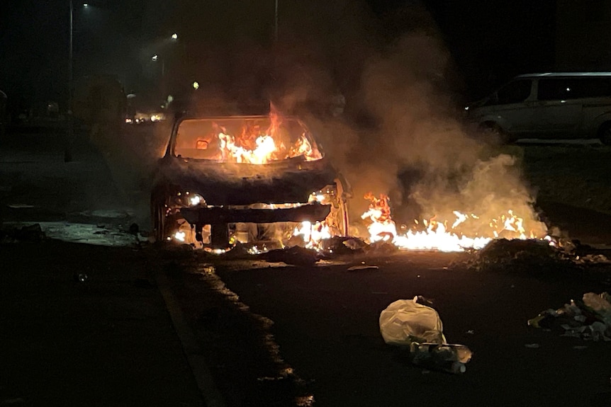 A car is ablaze in the middle of a road at night. 