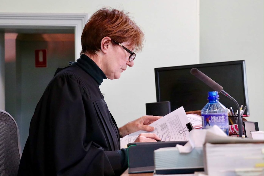 A woman sitting at a desk, looking at sheets of paper.